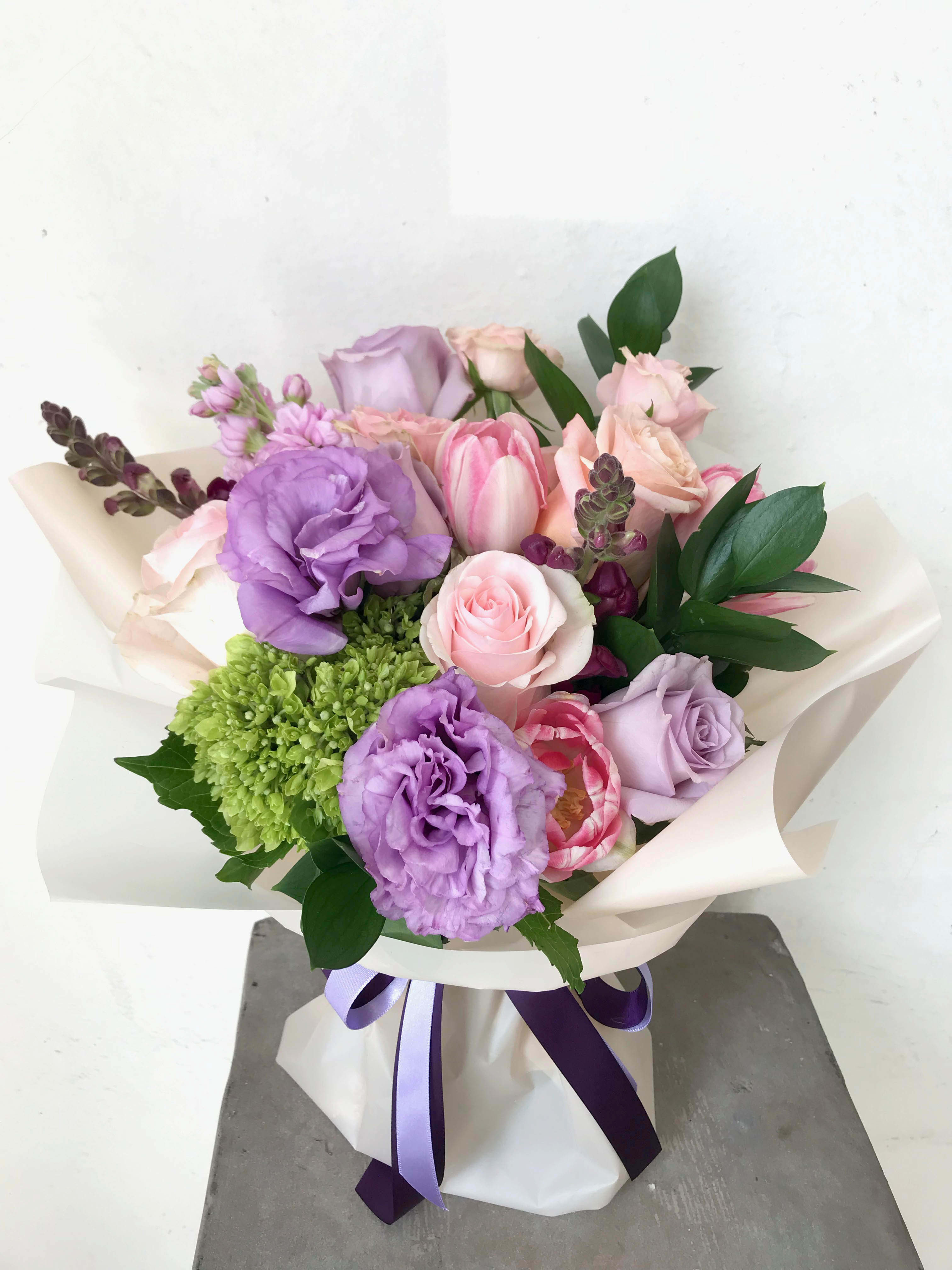 Bouquet of pink and lavender flowers wrapped in white paper with a purple ribbon