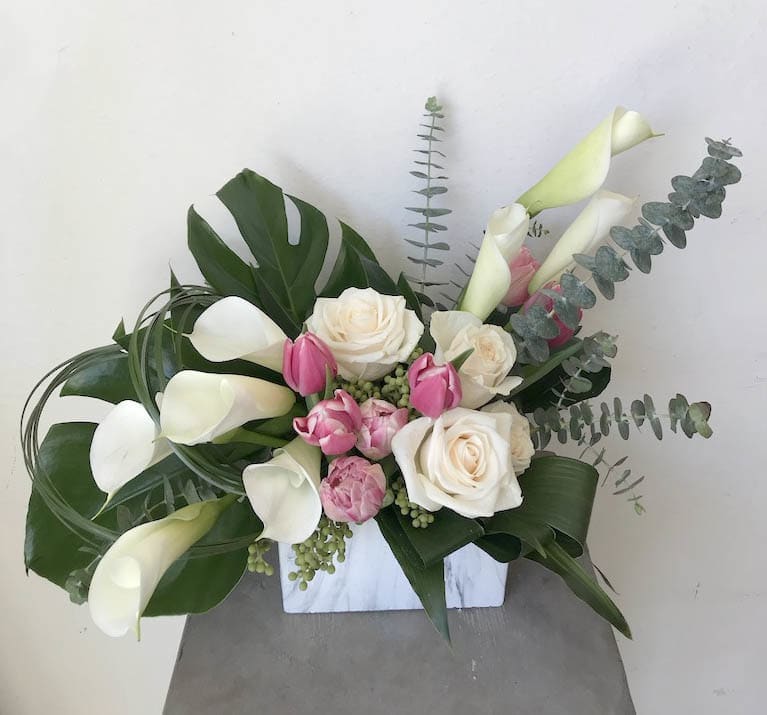 White calla lilies and roses with pink tulips in a white vase