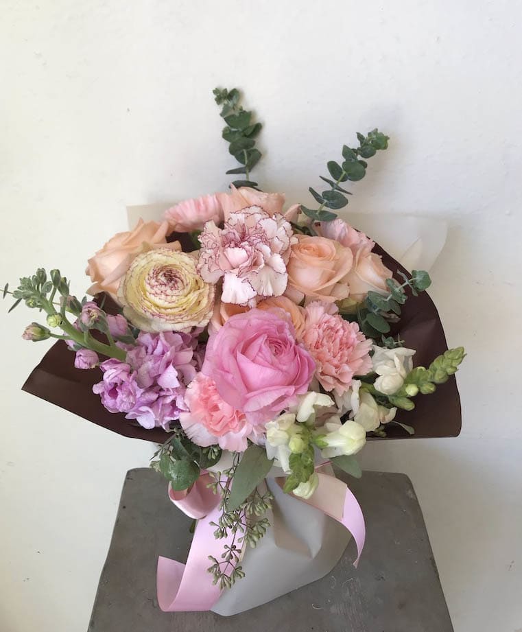 Bouquet of pink, peach, and white flowers wrapped in dark paper with a pink ribbon