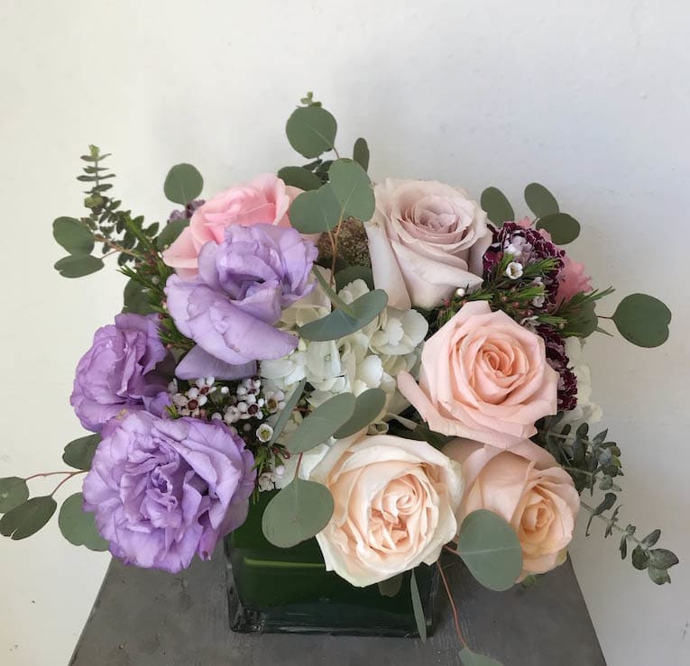 Bouquet of pink, peach, and lavender roses with eucalyptus in a square vase