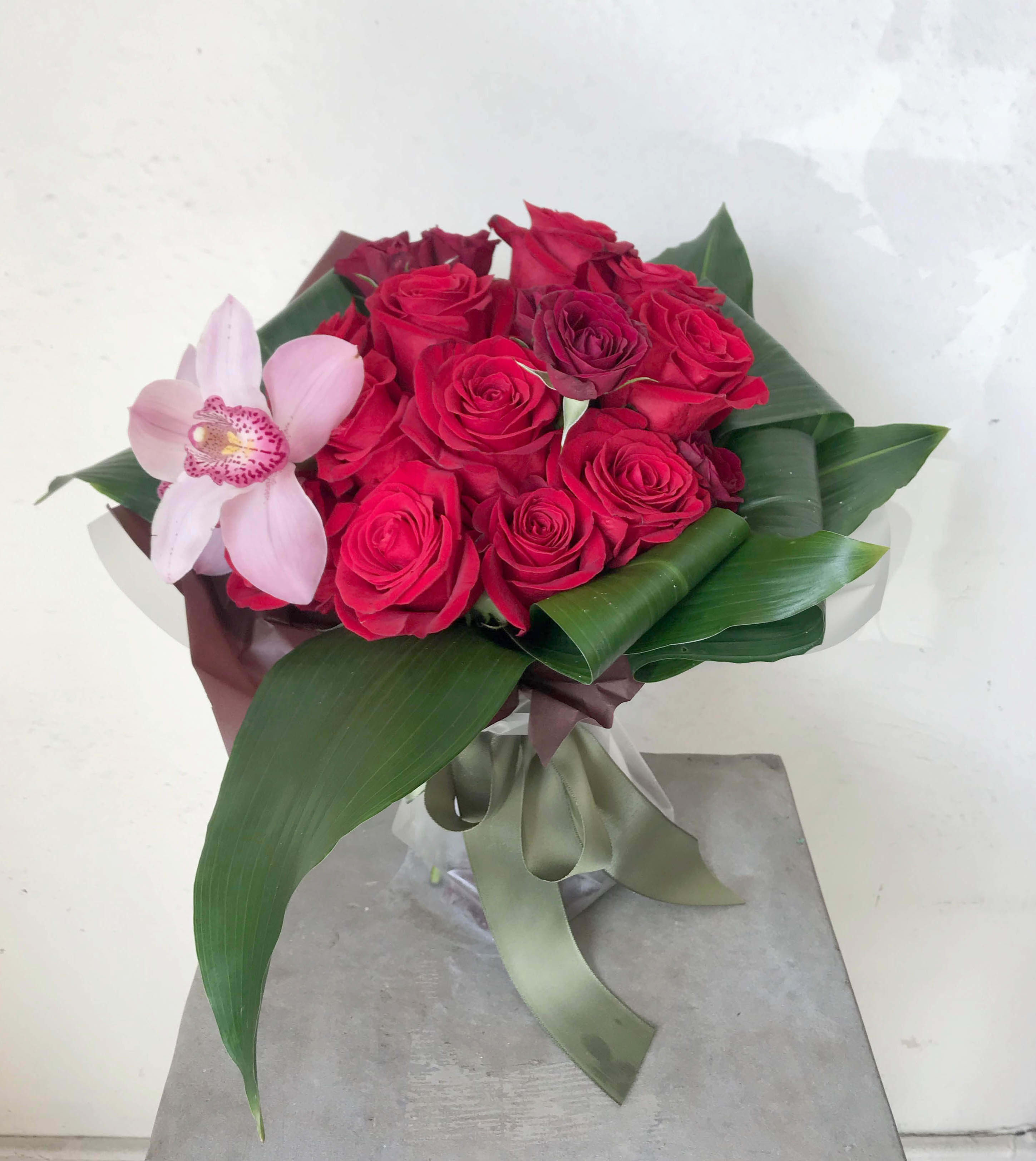 Bouquet of red roses with a pink orchid and broad green leaves