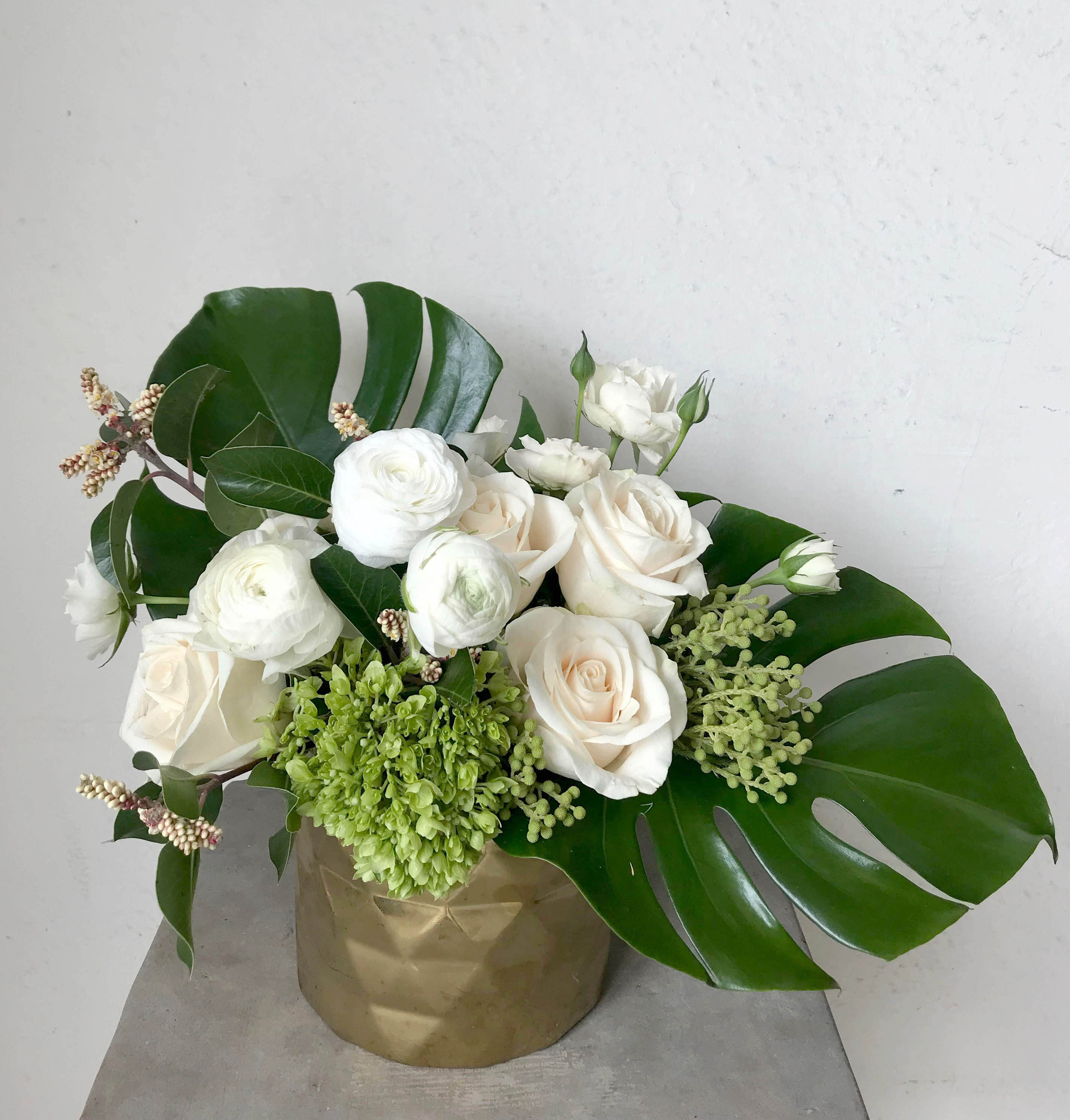 White roses and ranunculus in a gold vase with large tropical leaves