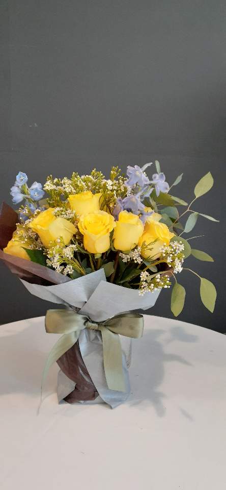 Yellow roses with small blue flowers in a wrapped bouquet