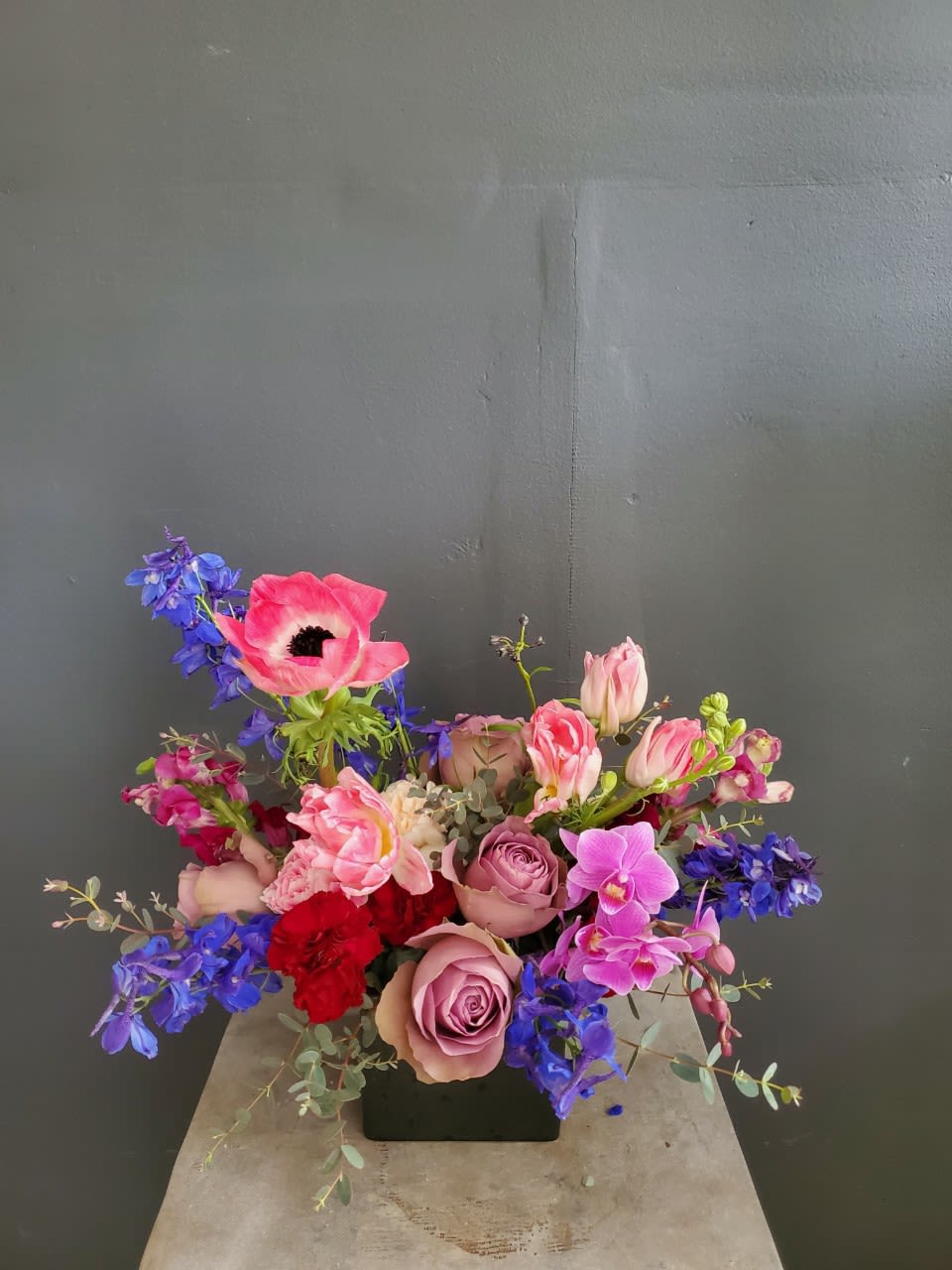 Mixed bouquet with pink roses, blue delphinium, and orchids in a black vase