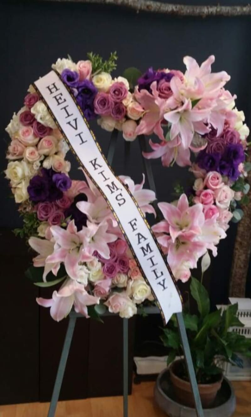 Heart-shaped floral wreath with pink lilies and roses on an easel