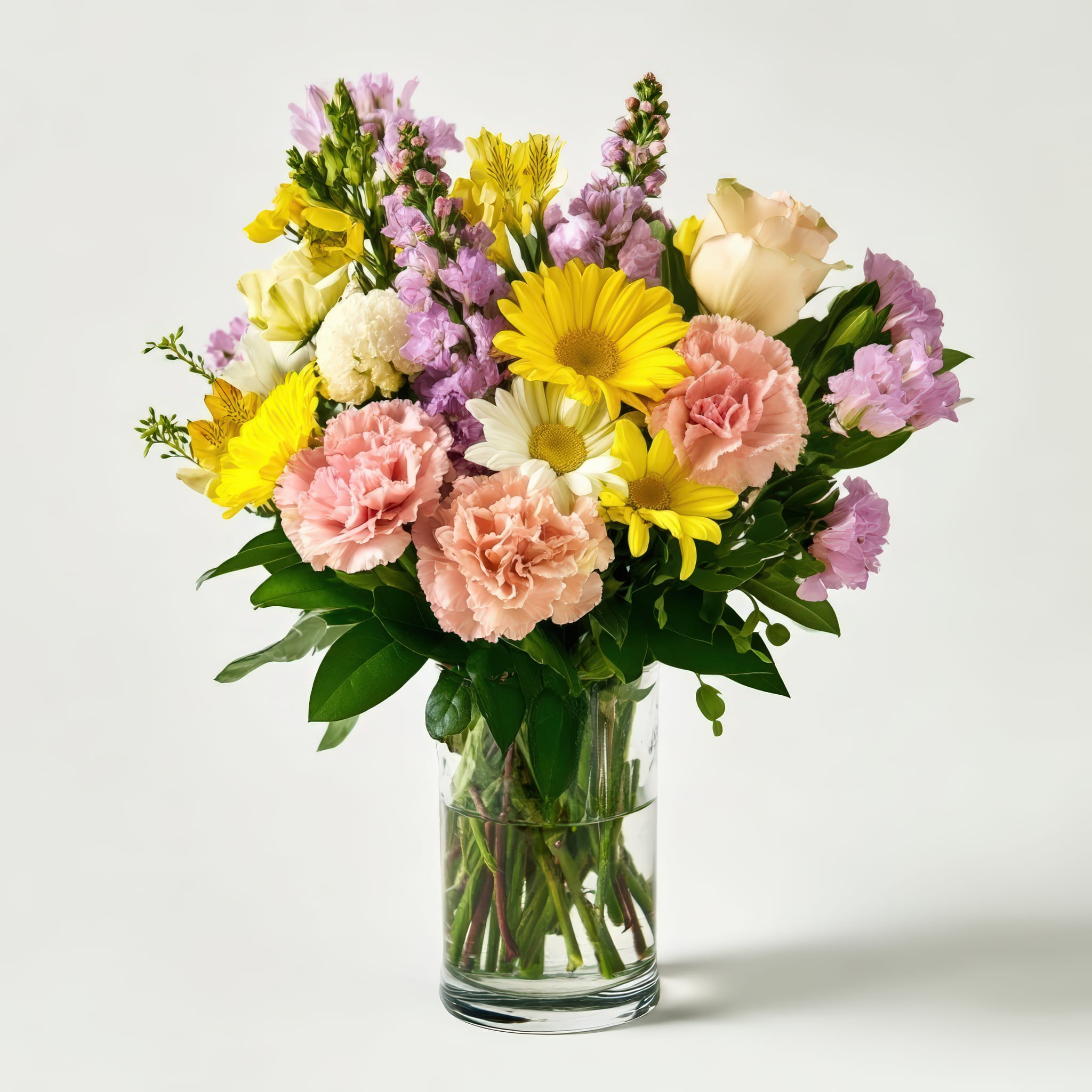 Mixed bouquet of yellow daisies, pink carnations, and purple flowers in a glass vase