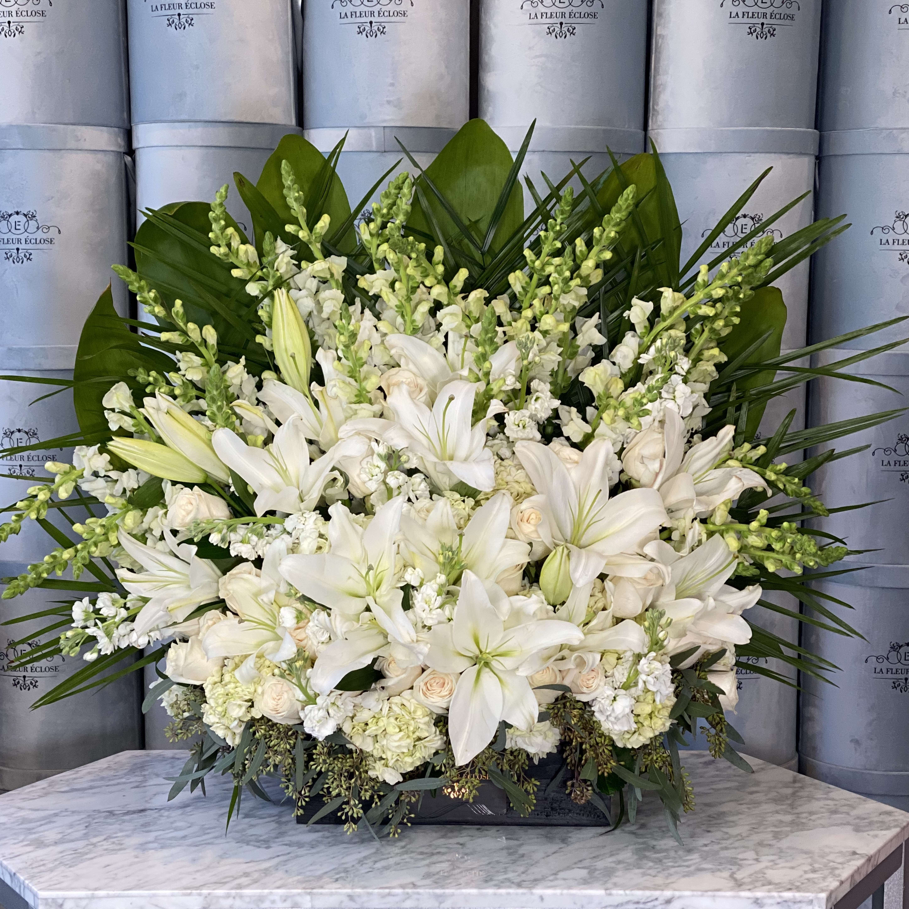 Large white floral arrangement with lilies and roses in a low container