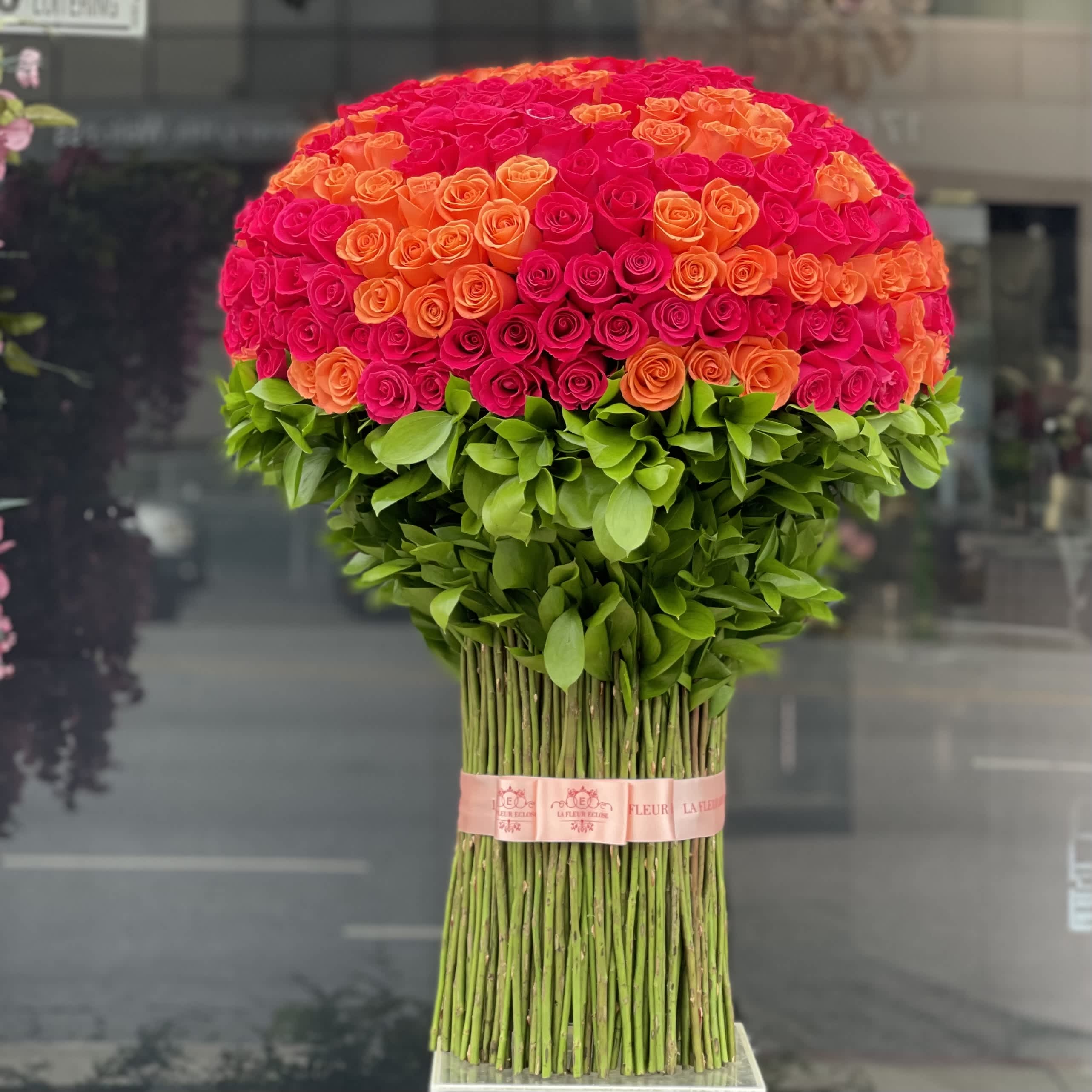 Large dome bouquet of pink and orange roses with a green leafy base