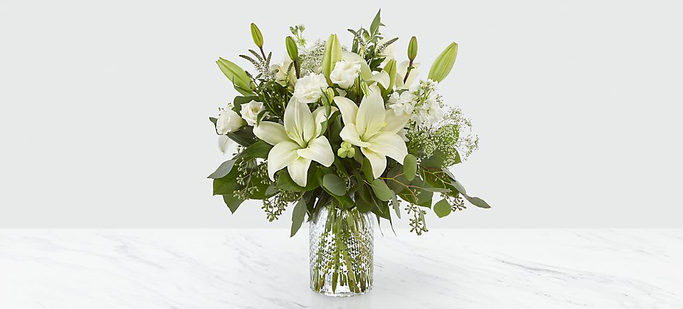 White lilies and roses arranged in a clear glass vase
