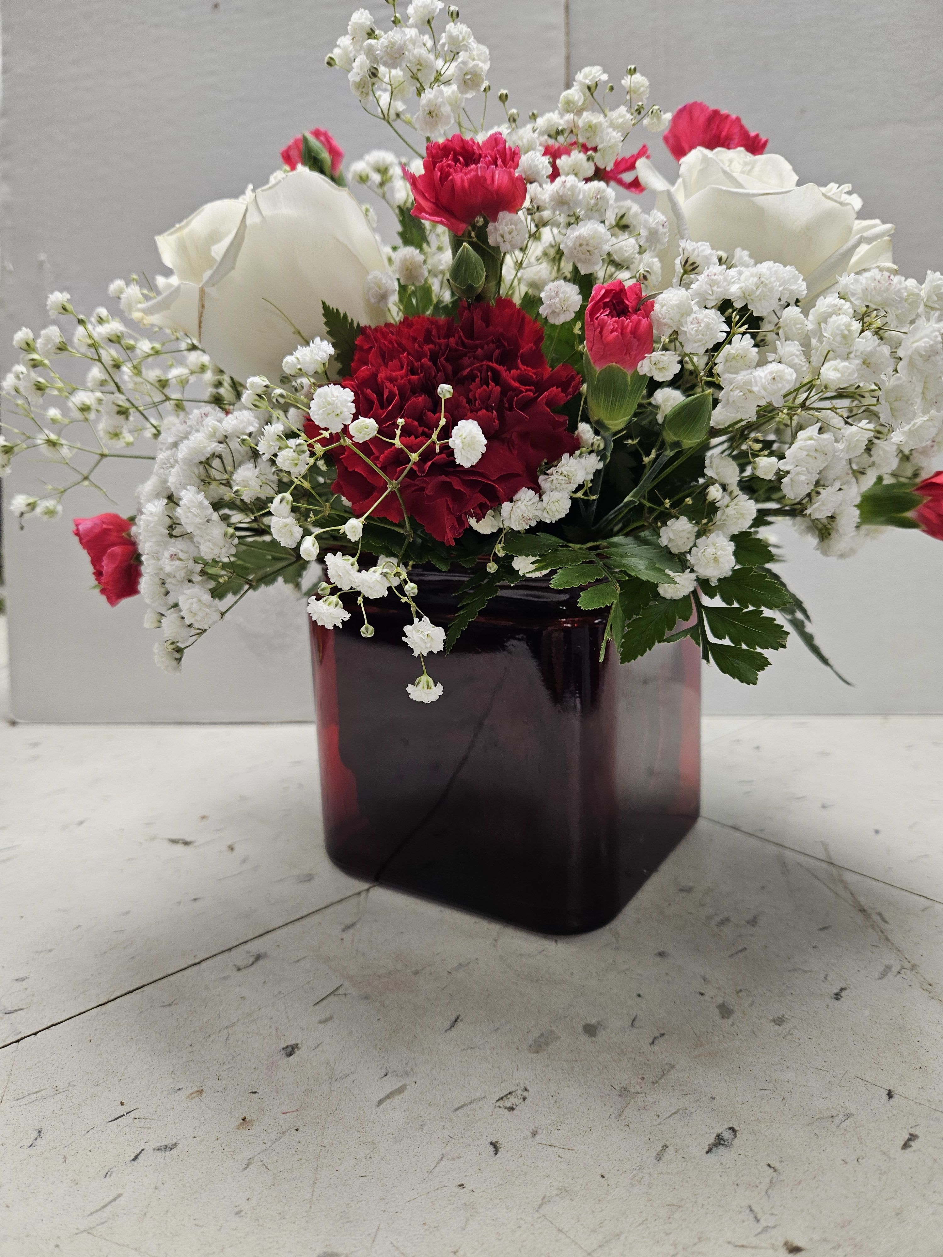 Red and white carnations with baby’s breath in a dark glass vase
