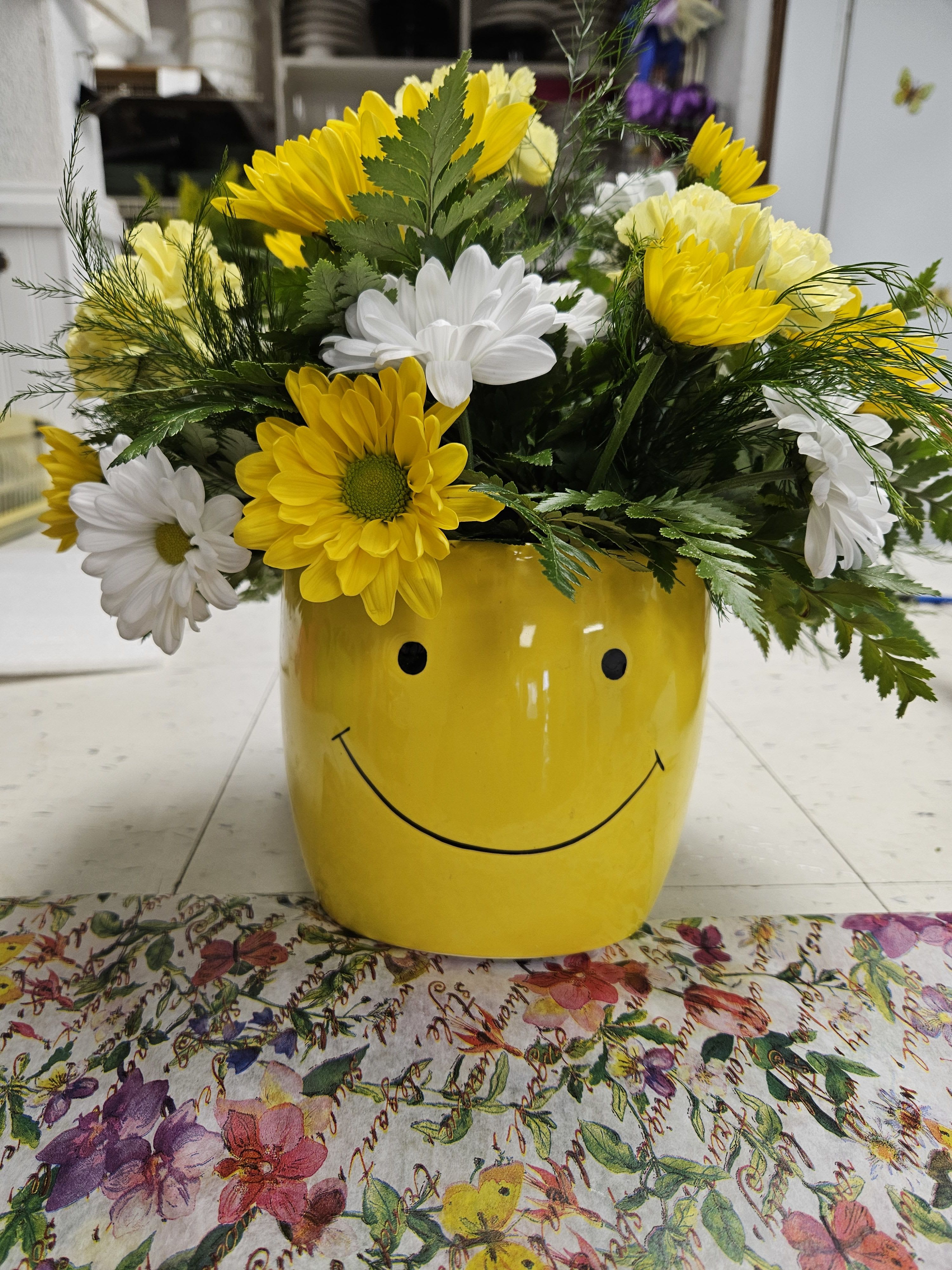 Yellow and white daisies in a smiley-face yellow pot