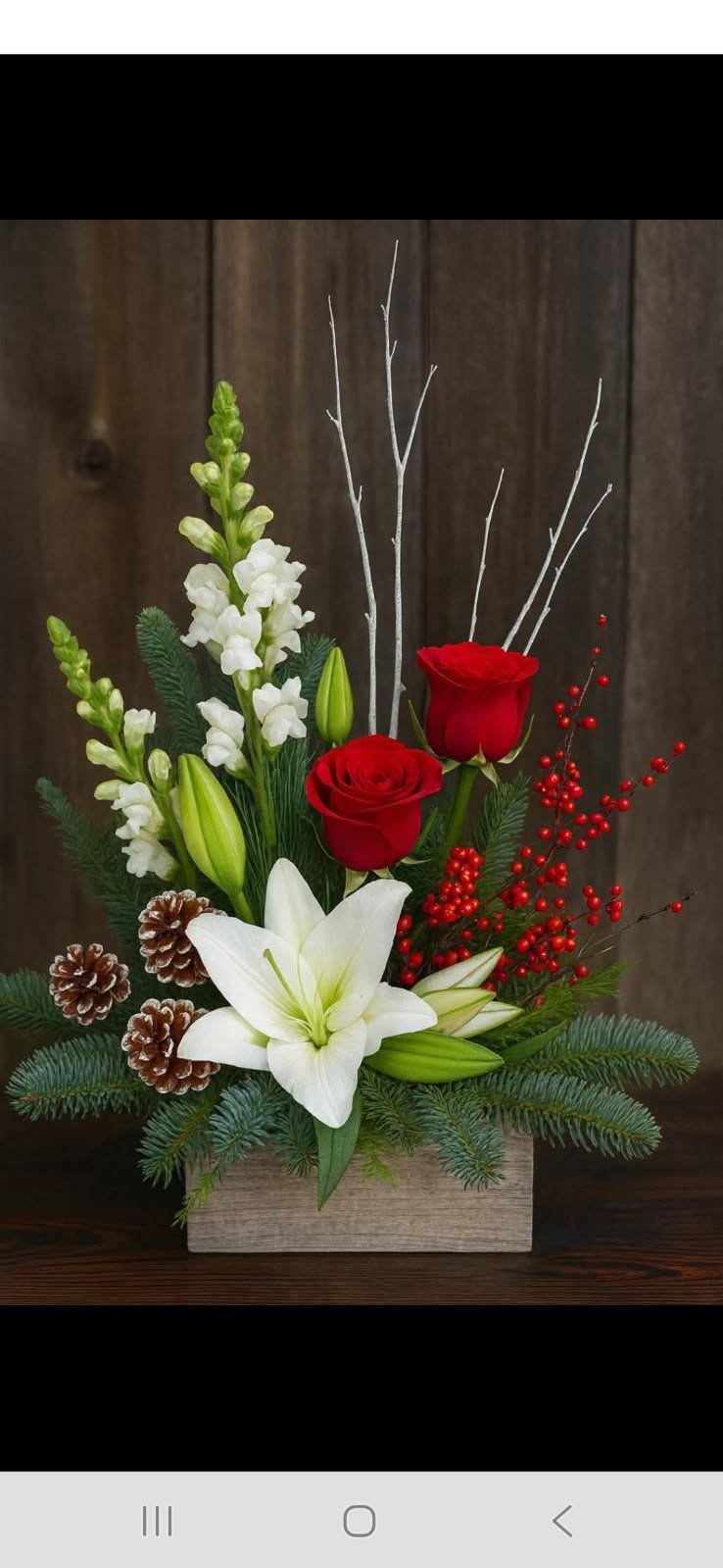 Holiday arrangement with red roses, white lilies, and pinecones in a wooden box