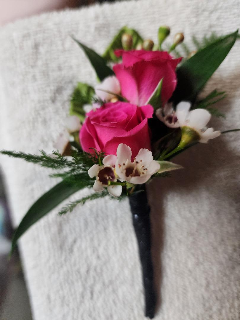 Pink rose boutonniere with white accent flowers and dark ribbon