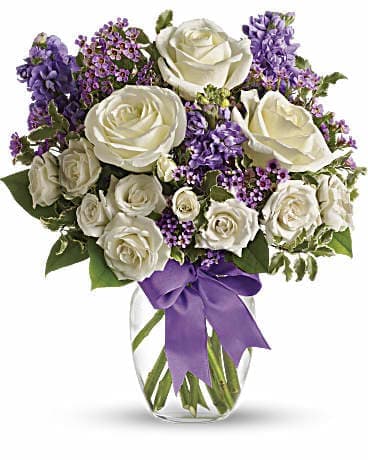 White roses and purple flowers in a clear glass vase with a purple ribbon