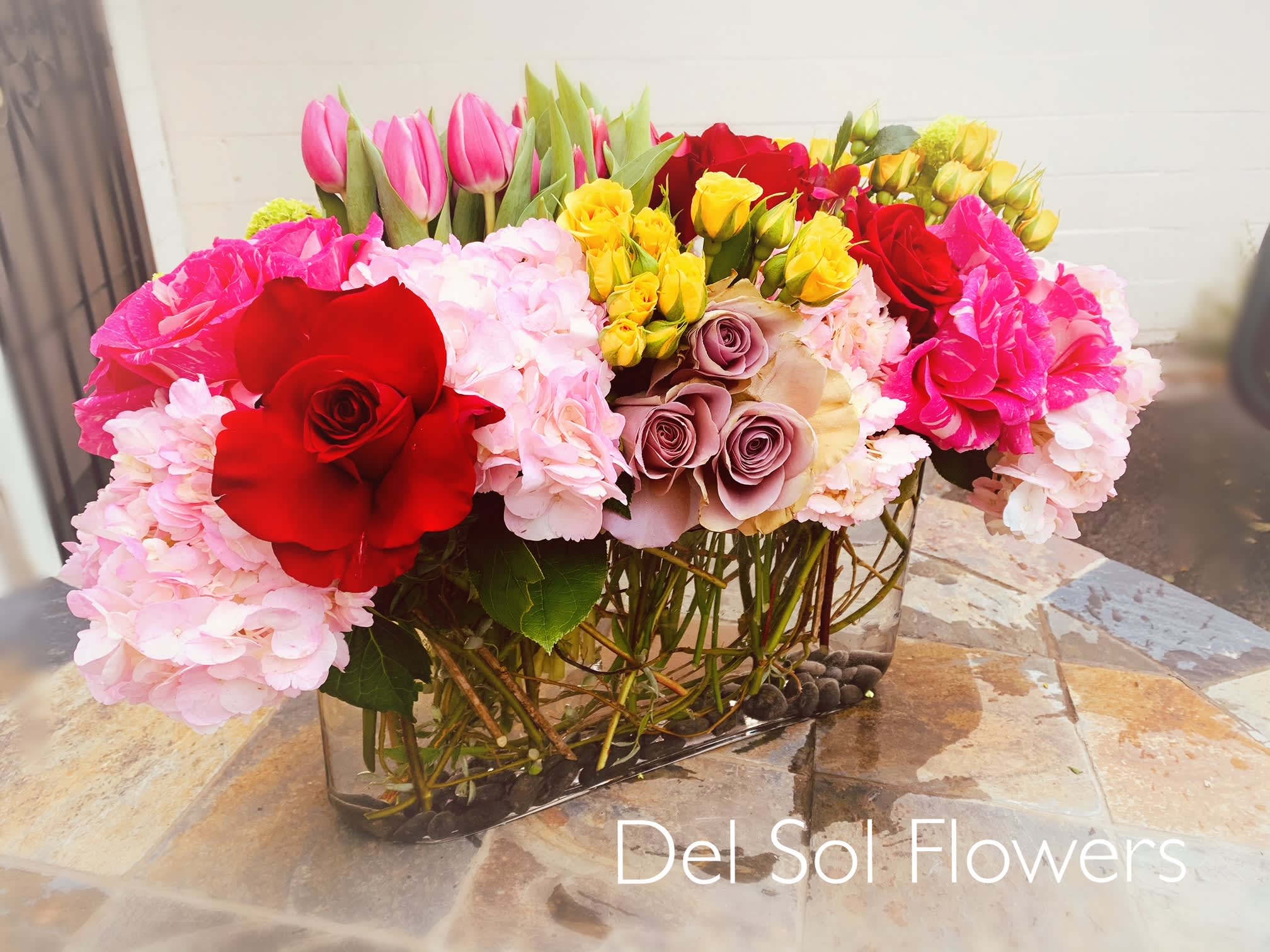 Mixed bouquet of roses, hydrangeas, and tulips in a glass vase