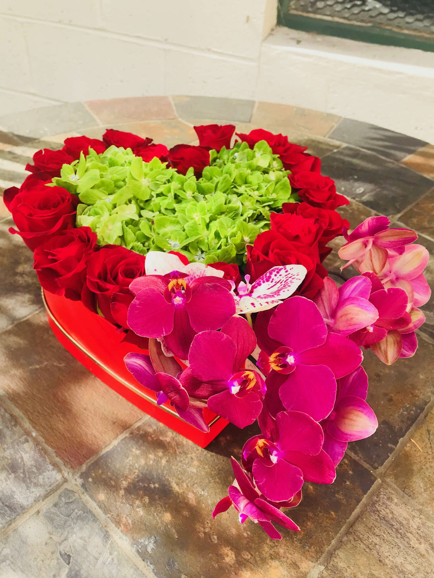 Heart-shaped arrangement of red roses and pink orchids with green hydrangeas