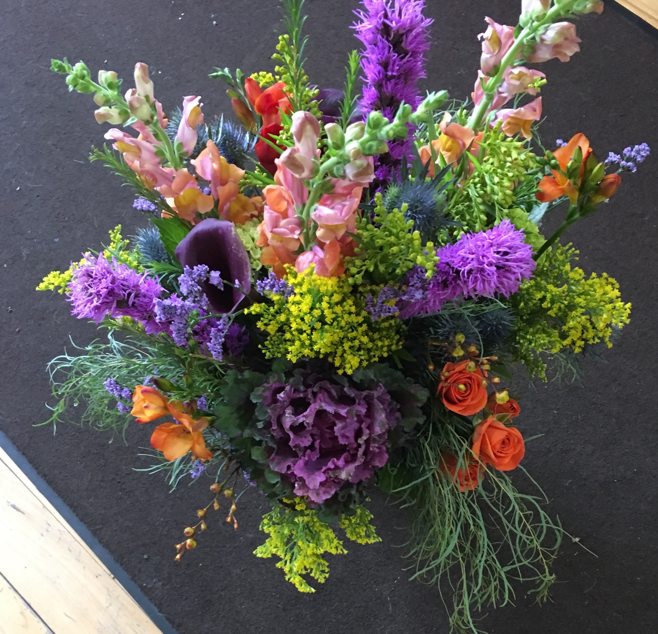 Tall mixed arrangement with purple, yellow, and orange flowers including snapdragons and roses