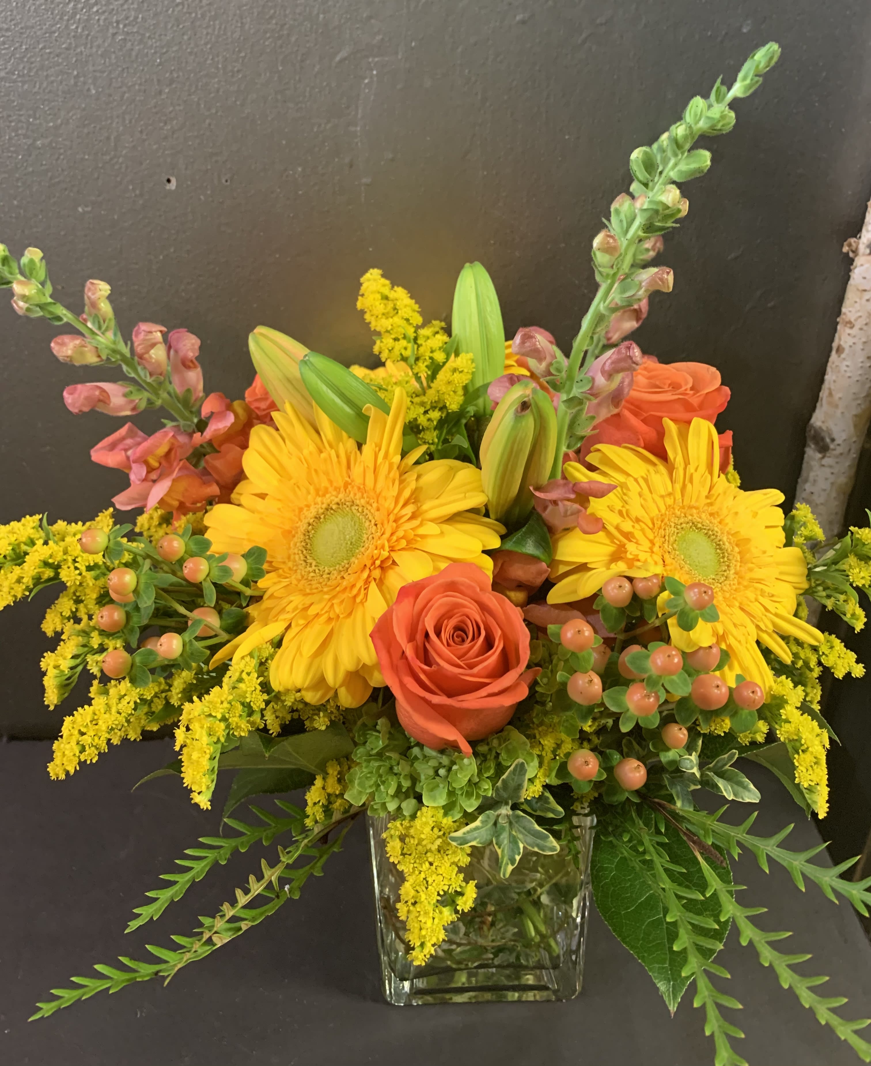 Bright yellow and orange flower arrangement in a clear glass vase