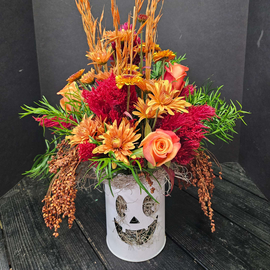 Orange and red floral arrangement in a white pumpkin vase