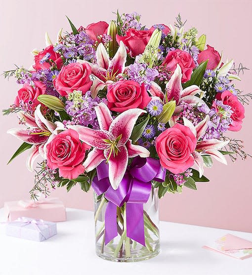 Pink roses and lilies in a glass vase with a purple ribbon