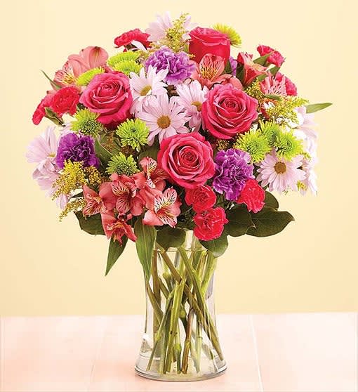 Mixed bouquet of pink roses, daisies, and carnations in a clear glass vase