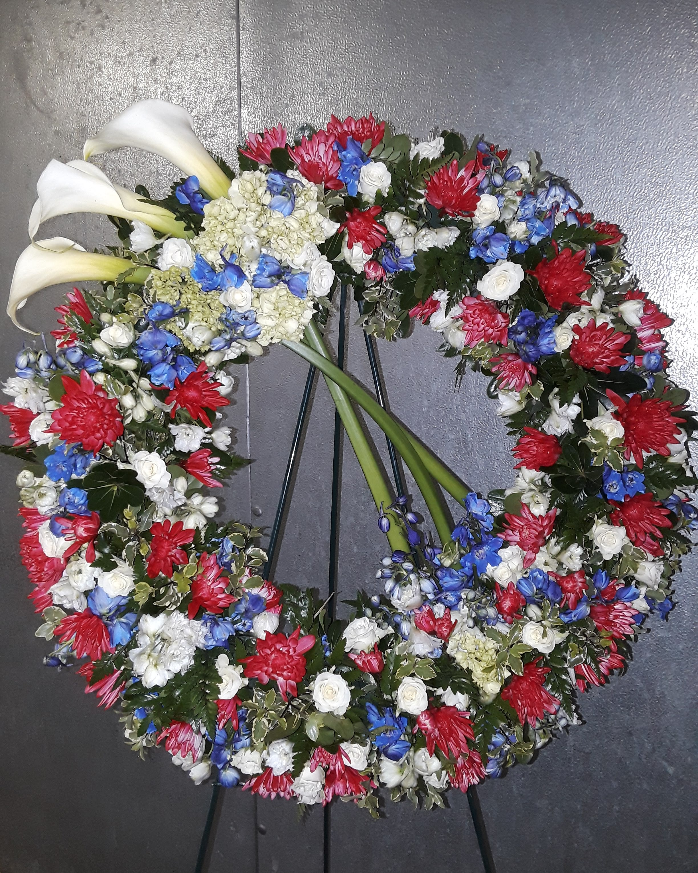 Circular floral wreath with white calla lilies and red, blue, and white blooms