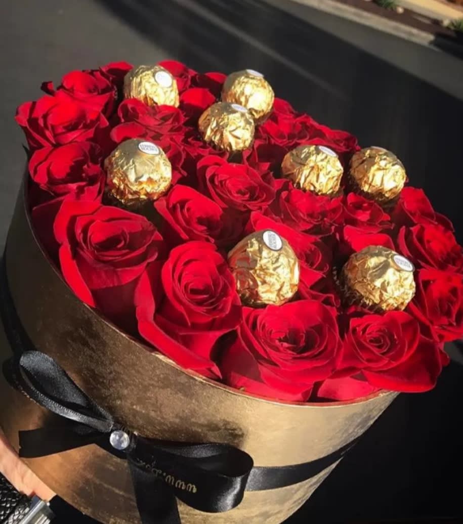 Red roses arranged in a round gold box with gold-wrapped chocolates on top