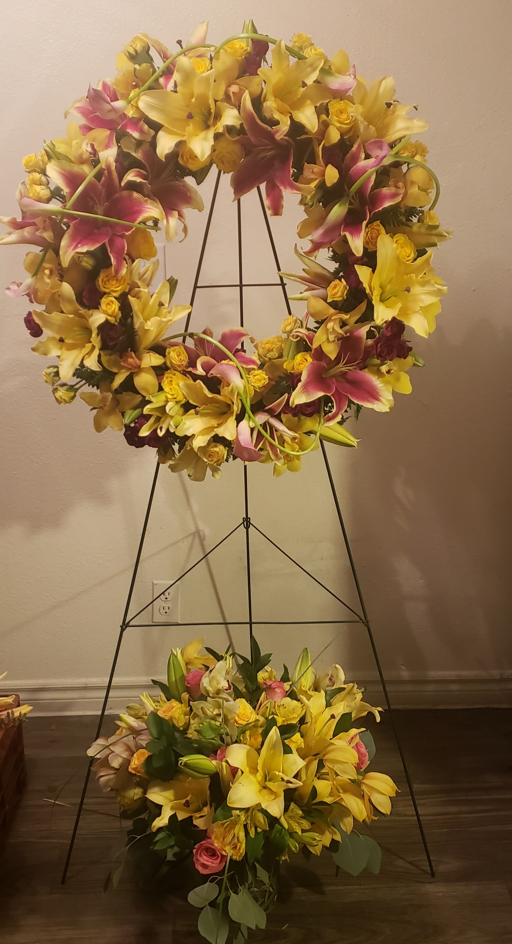 Large floral wreath on a black stand with yellow lilies and pink flowers