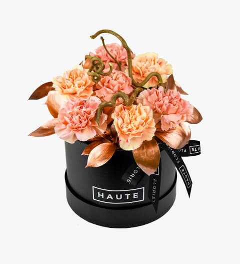 Peach carnations arranged in a black round box with ribbon