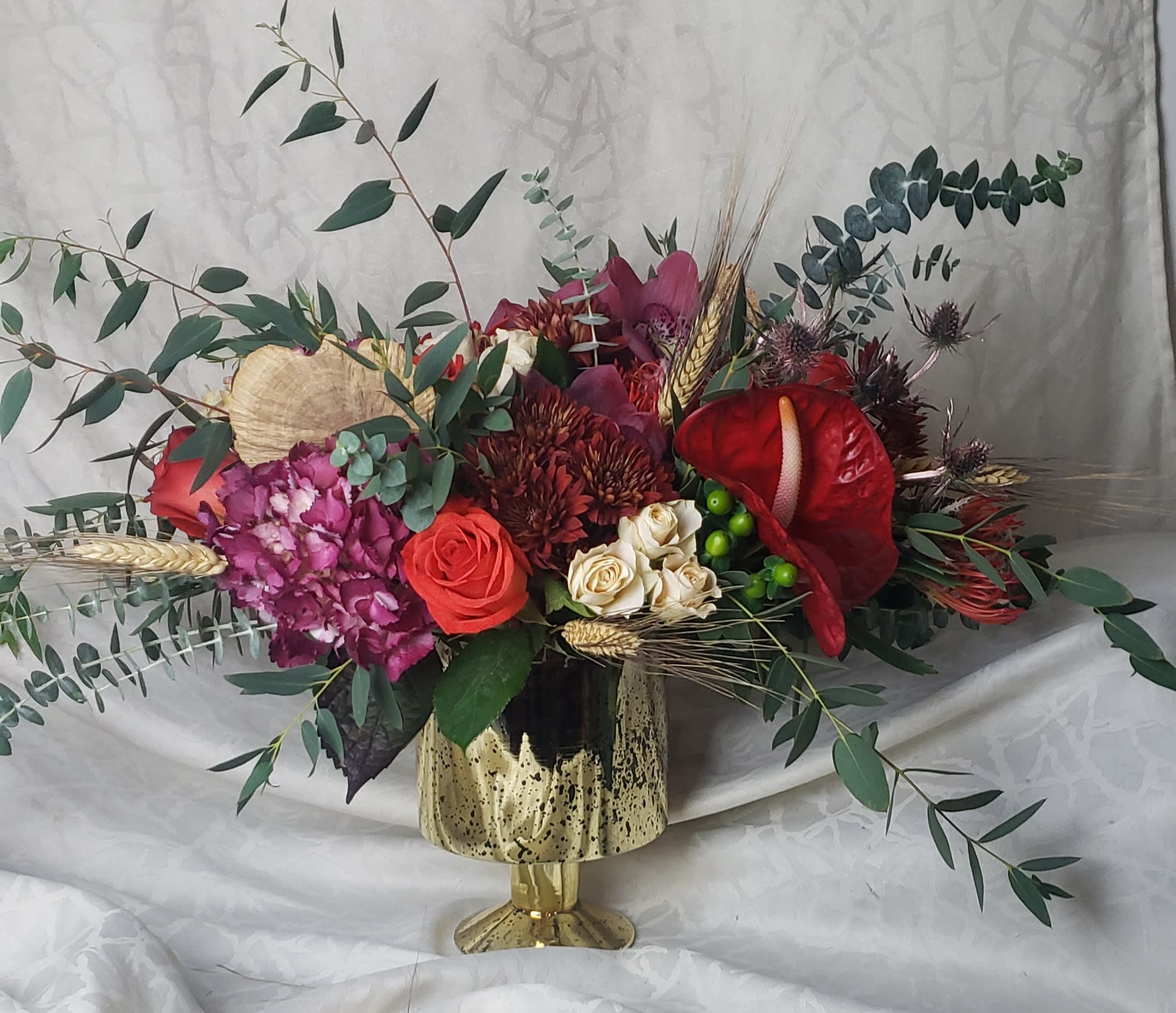 Mixed floral arrangement in a gold vase with red and pink blooms