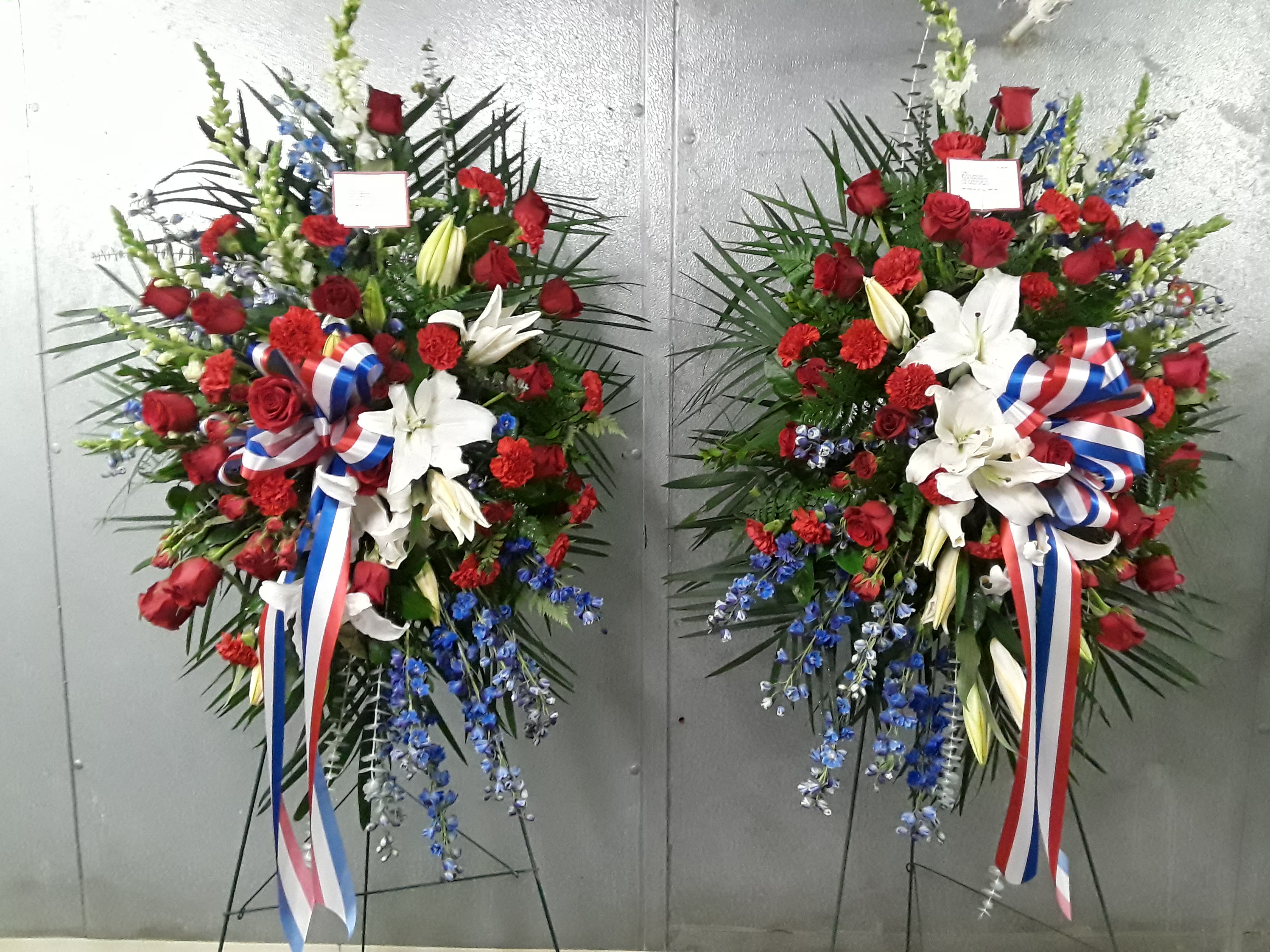 Two large standing floral sprays with red roses, white lilies, and blue accents