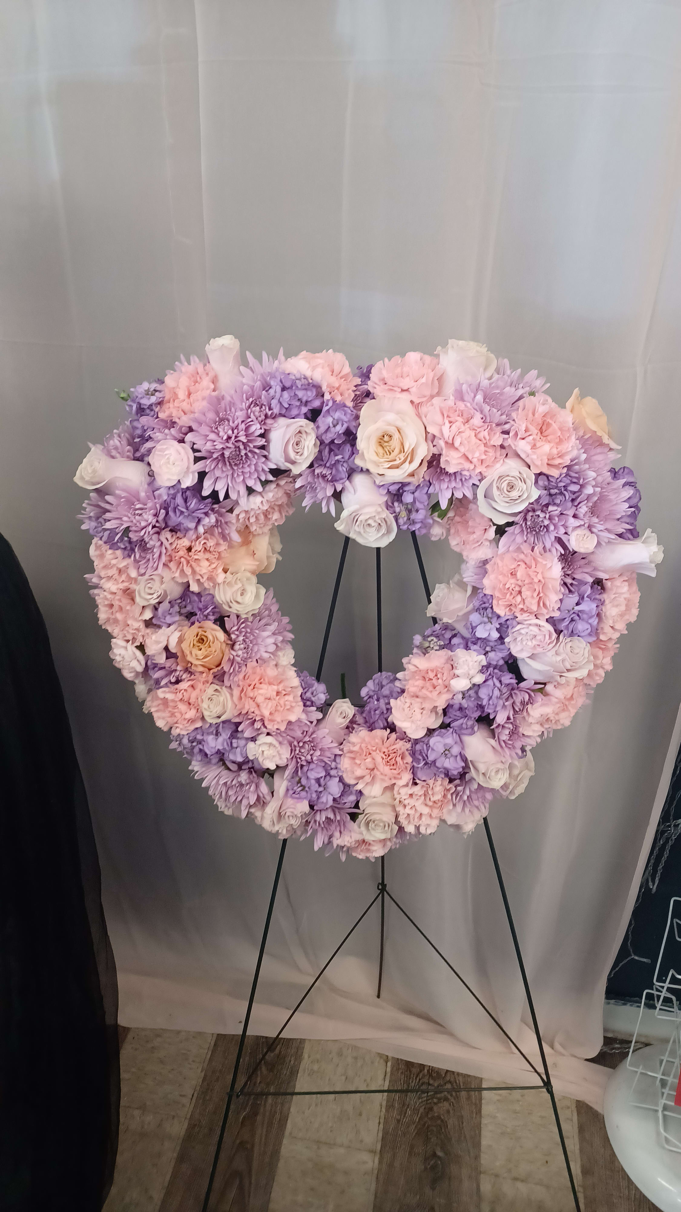 Heart-shaped floral wreath in pink, lavender, and white on a stand