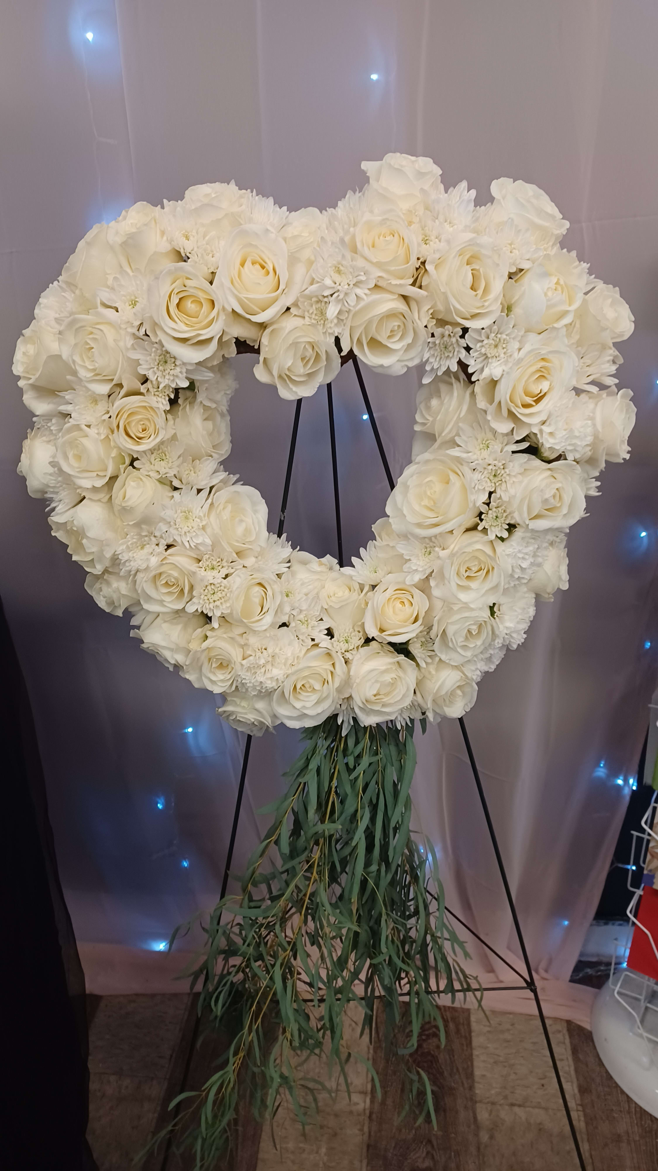 Heart-shaped white floral wreath on a stand with trailing greenery