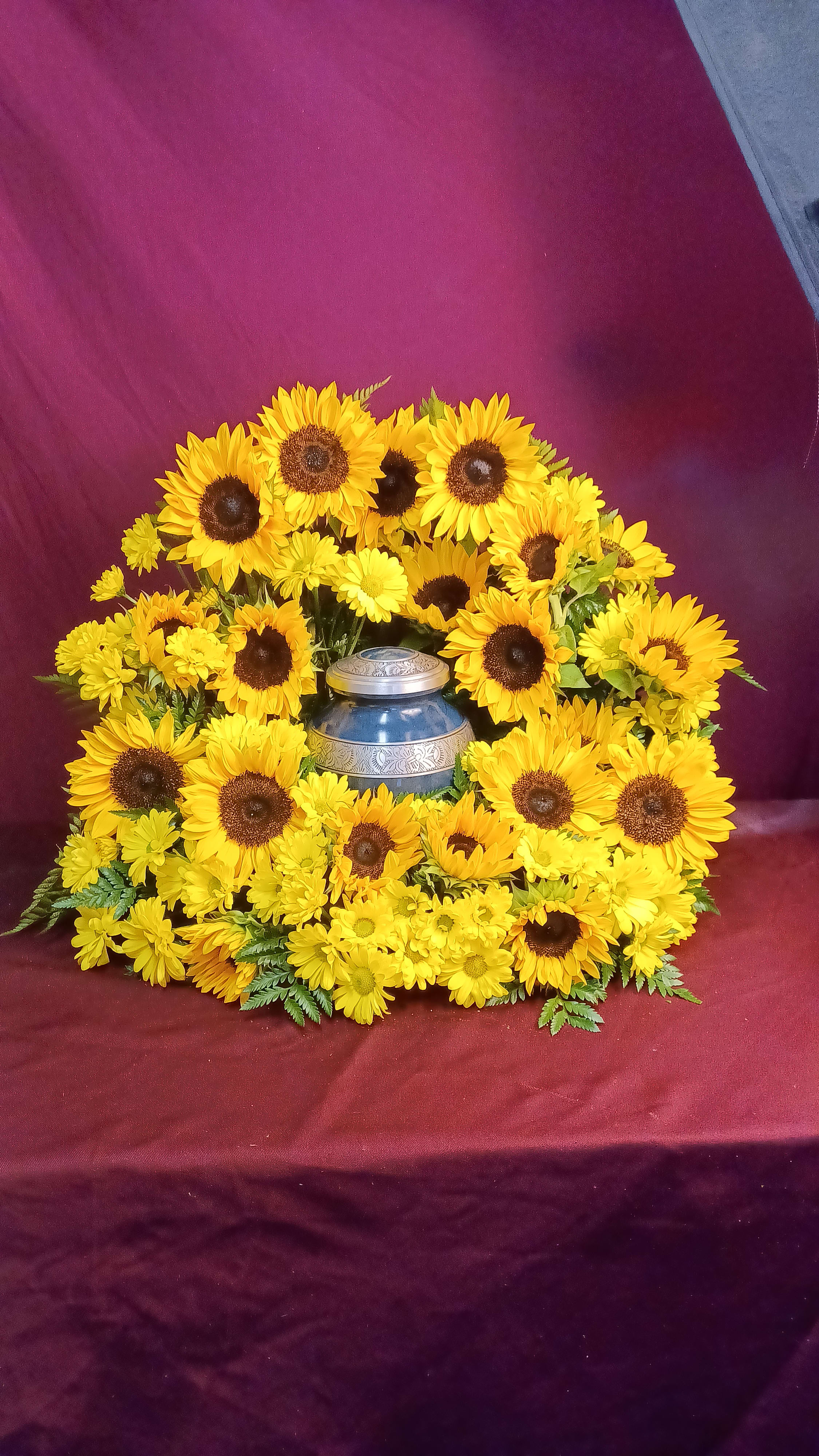 Yellow sunflowers arranged around a blue urn on burgundy fabric
