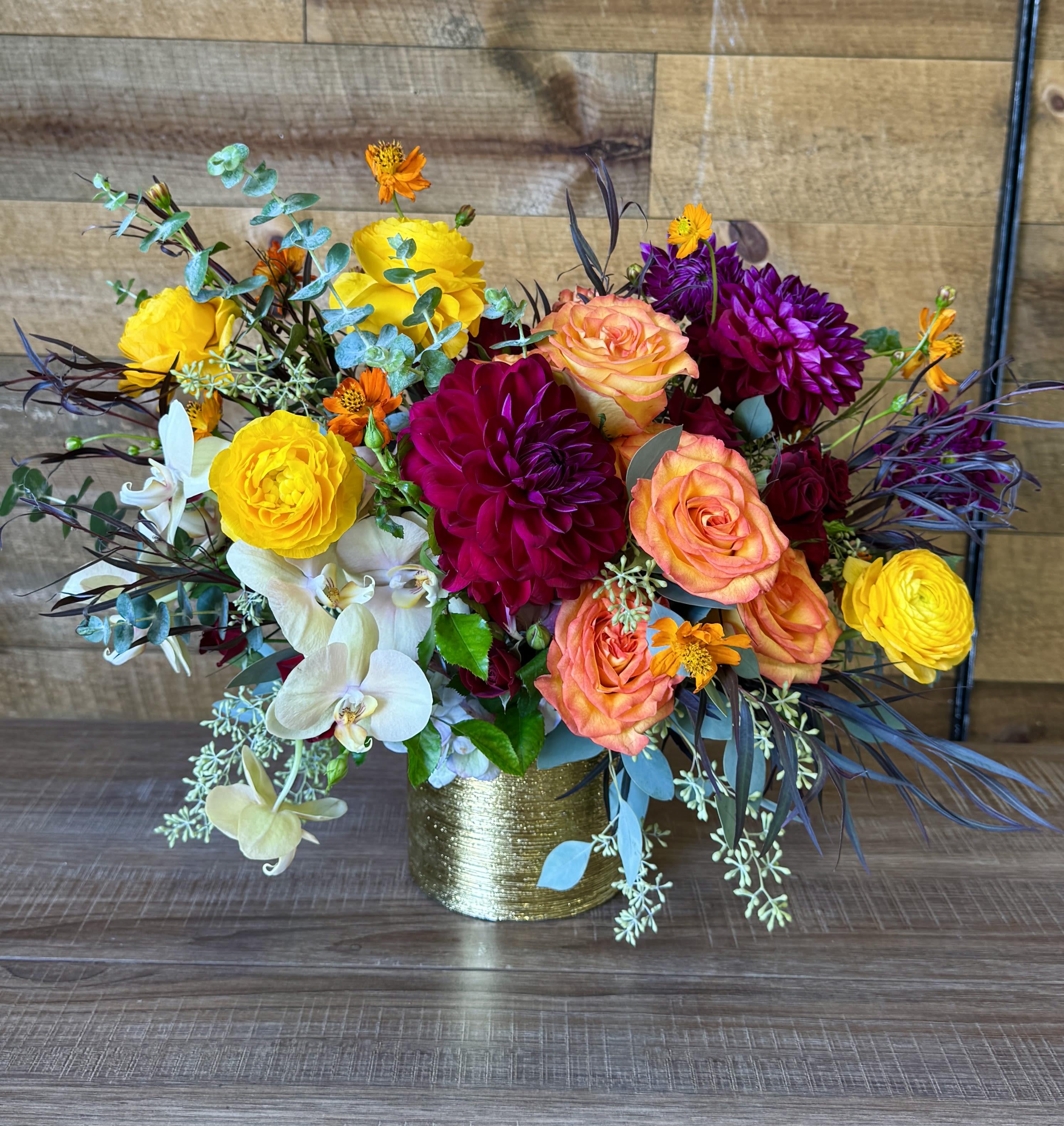 Colorful bouquet of roses, orchids, and dahlias in a gold vase