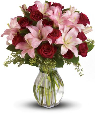 Arrangement of pink lilies and red roses in a clear glass vase with water.