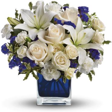 White lilies and roses with blue accents in a cobalt glass cube vase