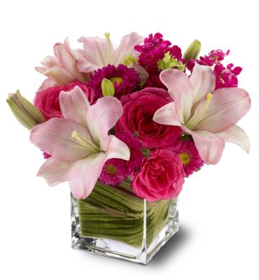 Pink lilies and roses arranged in a clear square vase