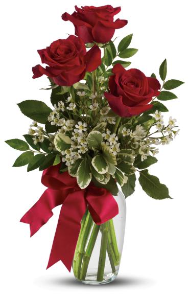 Three red roses with small white blossoms in a clear glass vase tied with a red ribbon
