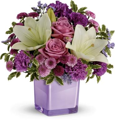 Lavender and purple arrangement with lilies, roses, carnations, and mums in a square lavender glass vase