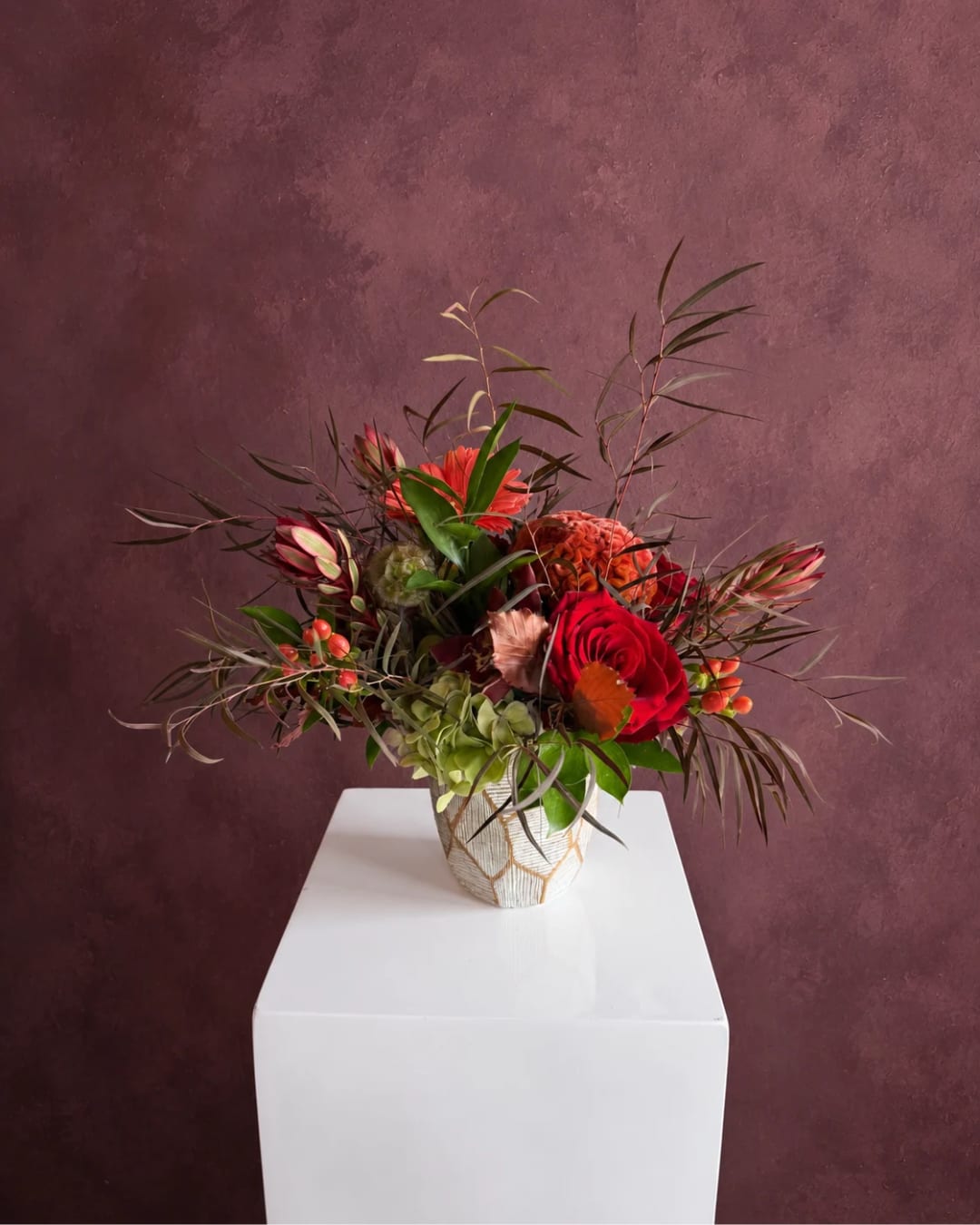 Mixed floral arrangement with red roses in a patterned vase