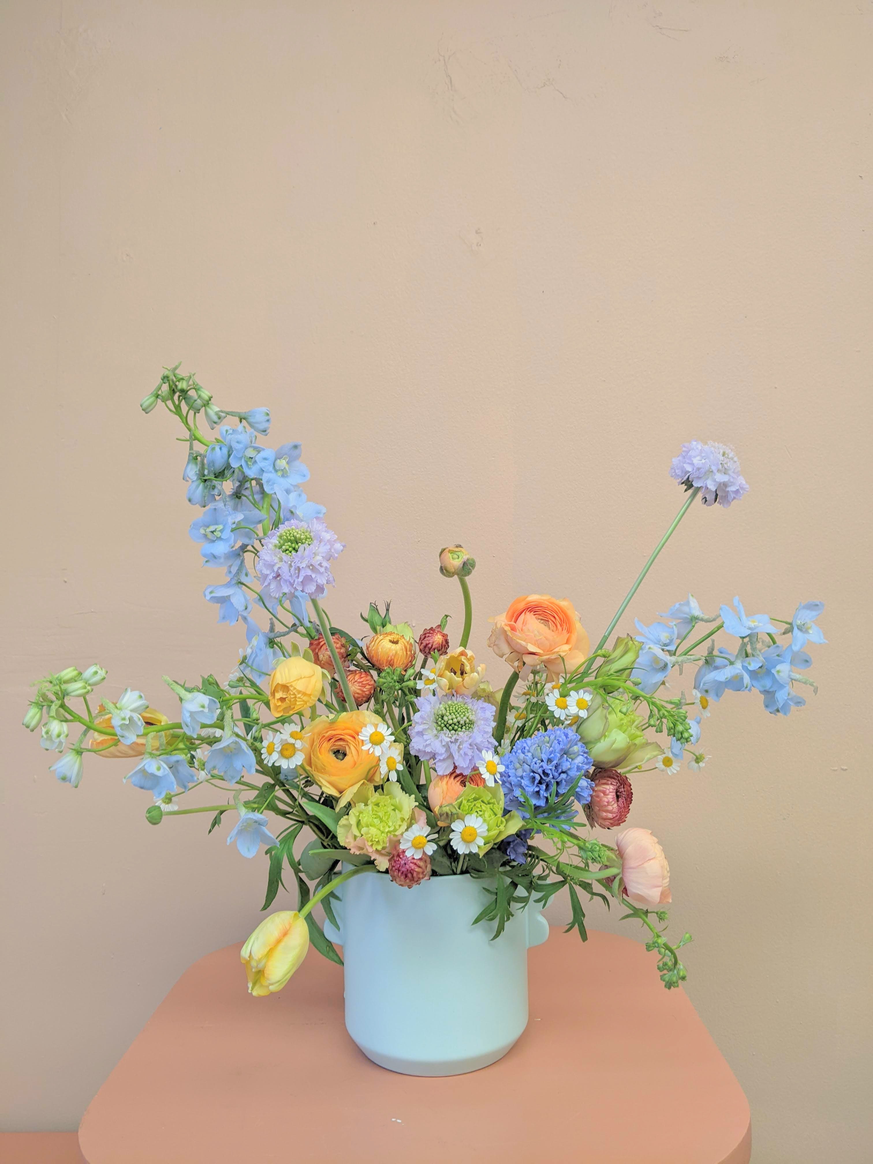 Pastel mixed bouquet in a light blue vase with blue and yellow blooms