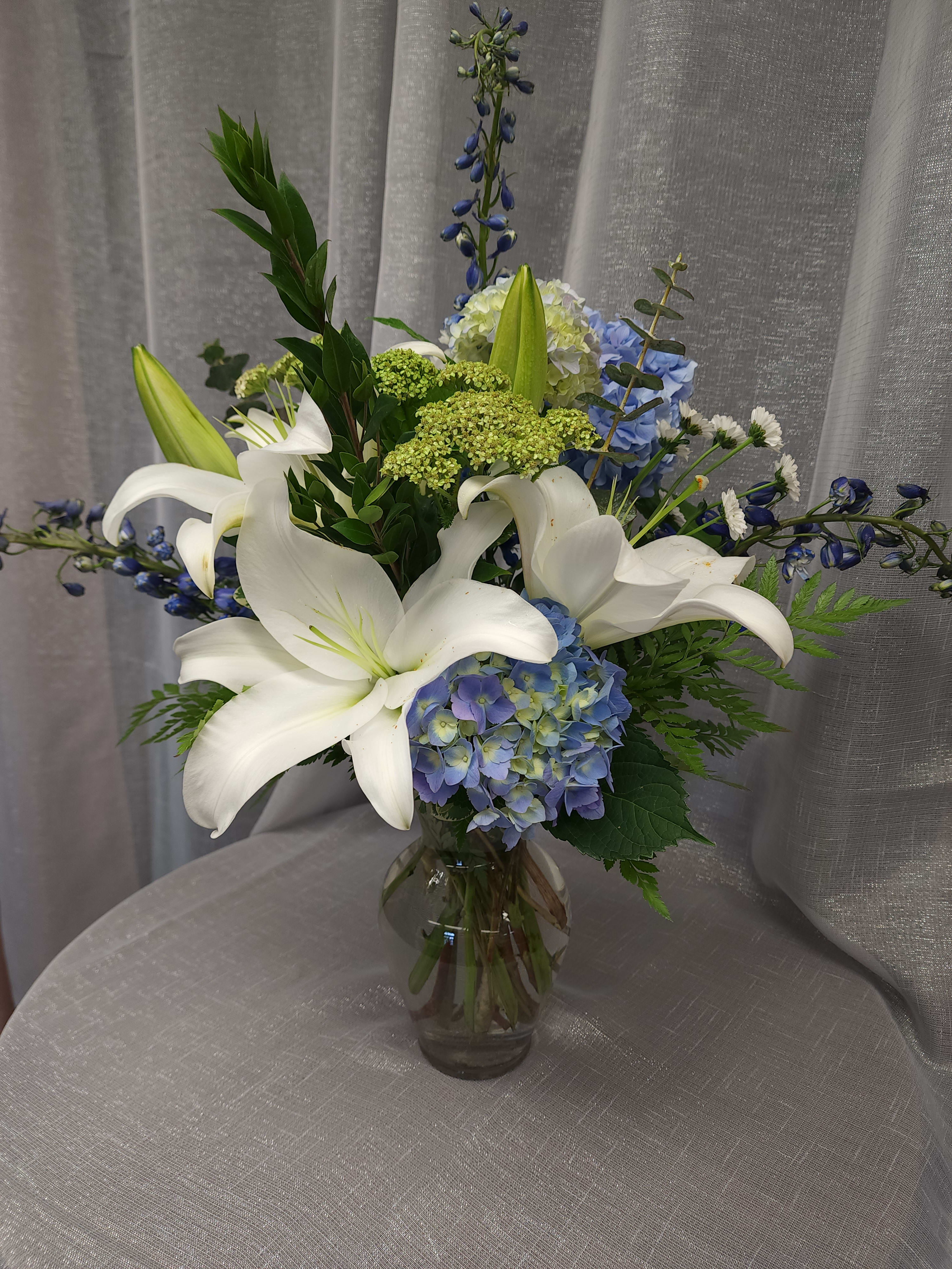 Breezy by the Sea by MG Florist - This arrangement contains delphinium, asiatic lilies, hydrangea, and other seasonal blooms. It is a great gift for a birthday, get well, for wishing someone a fresh start. APPROXIMATE DIMENSIONS: 15" D x 18" H