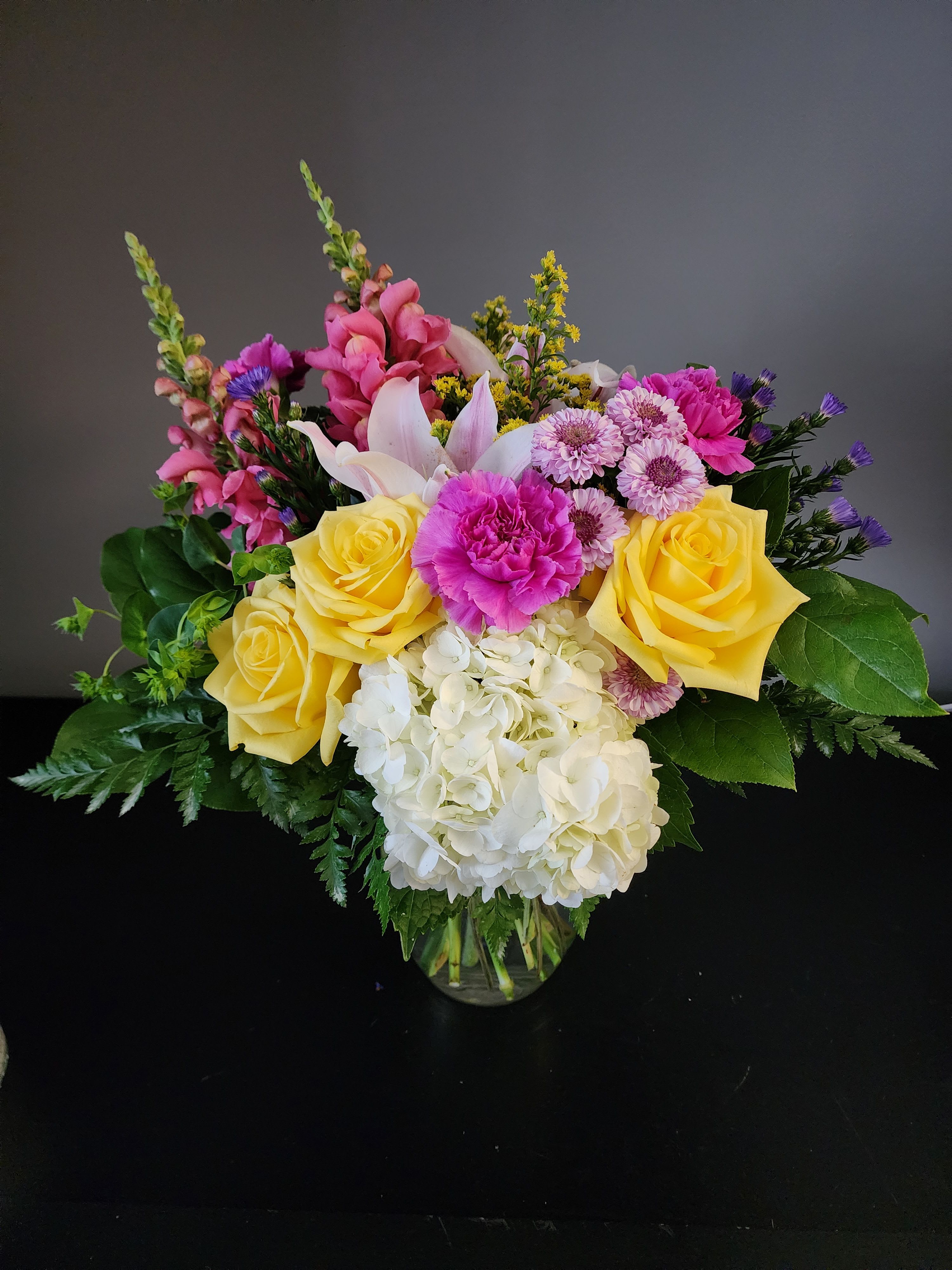 Mixed bouquet of yellow roses, pink blooms, and white hydrangea in a glass vase