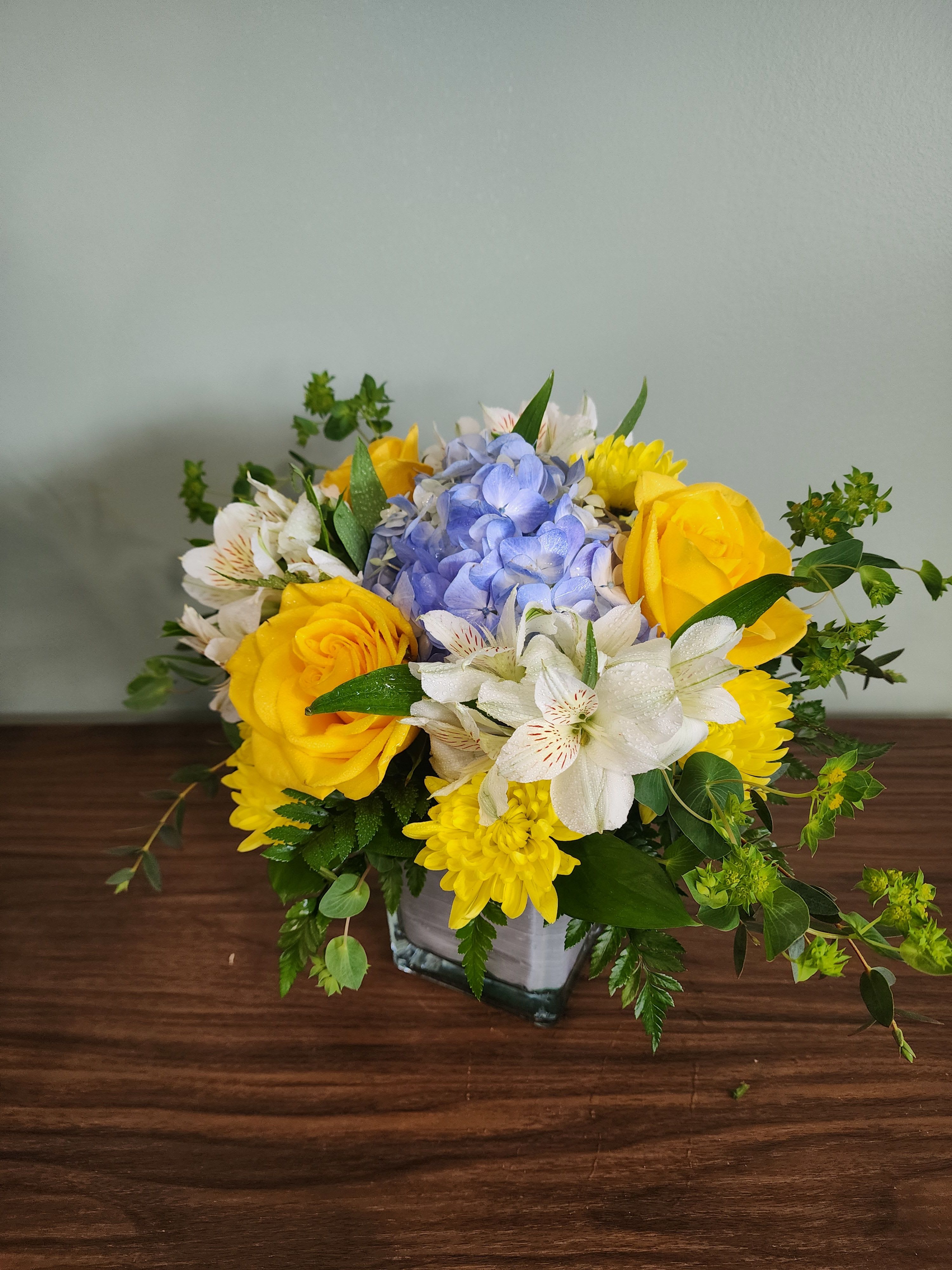 Yellow roses and white alstroemeria with blue hydrangea in a glass vase