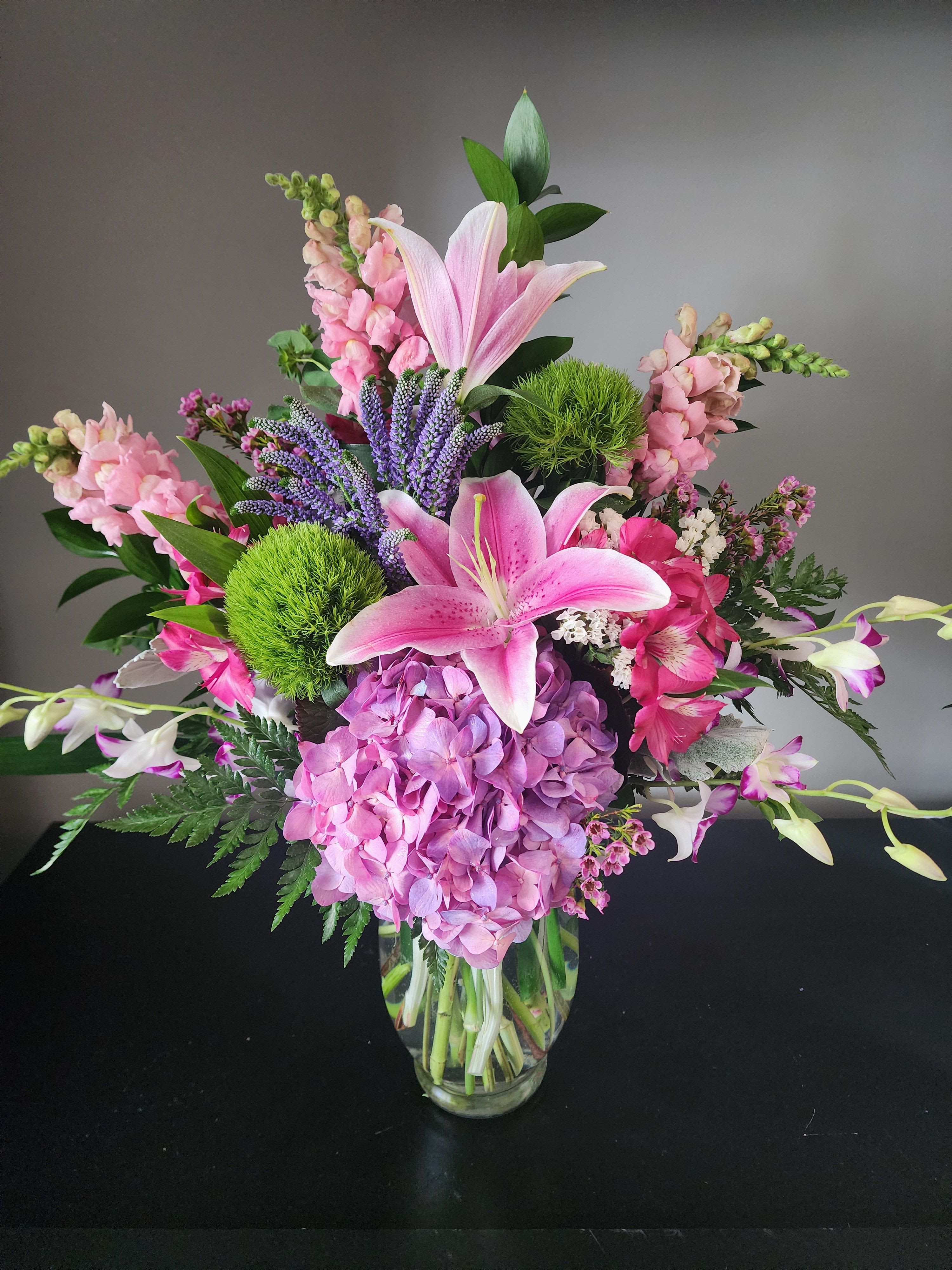 Pink lilies and hydrangea in a glass vase with purple spikes