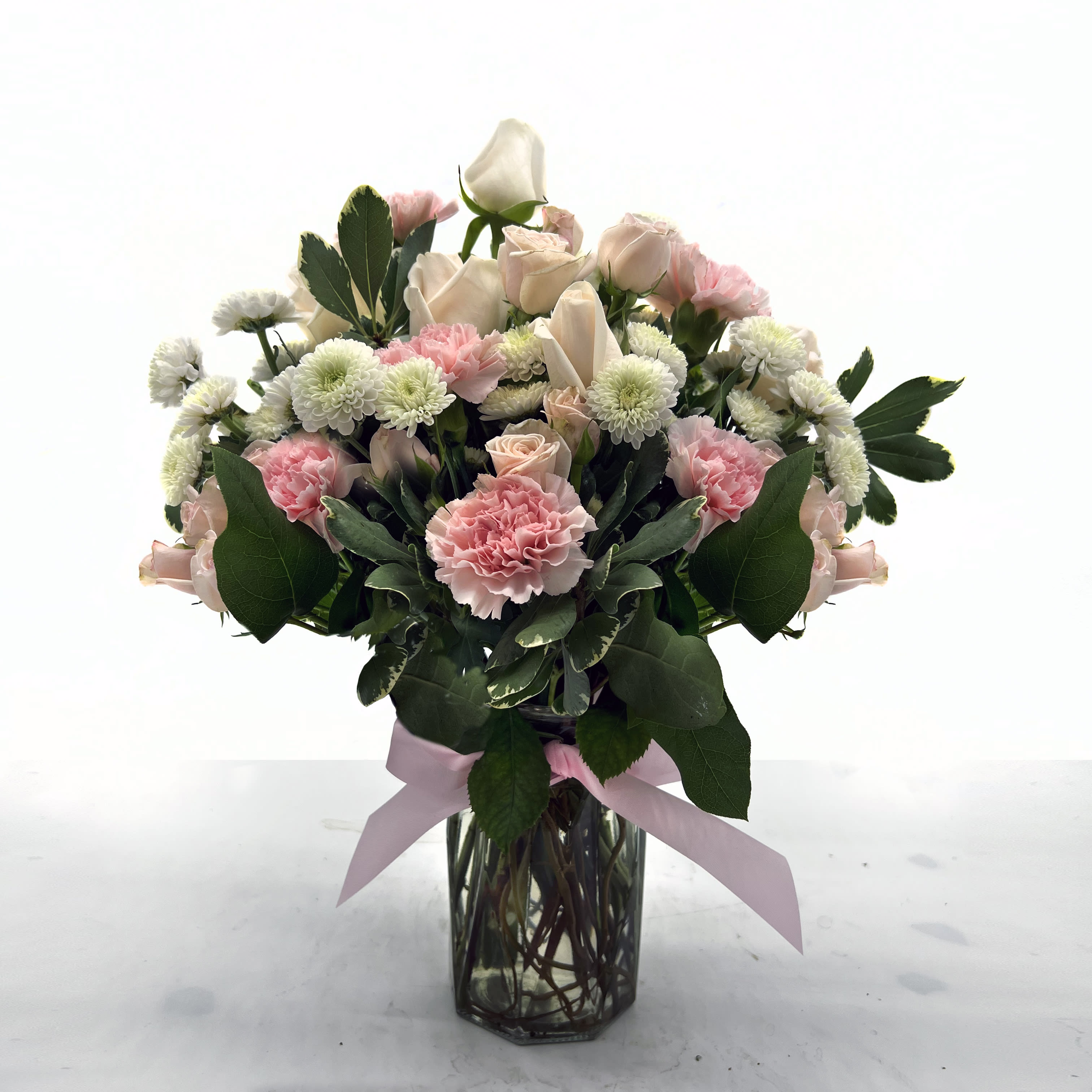 Pink roses and carnations arranged in a glass vase with a ribbon