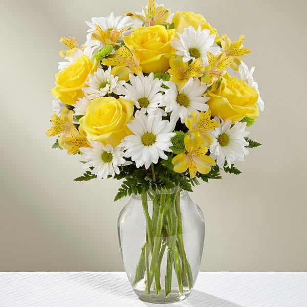 Yellow roses and white daisies in a clear glass vase