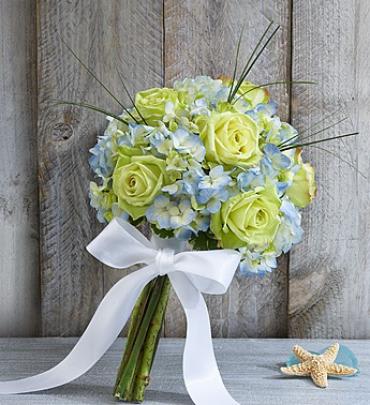 Beach Wedding Rose and Hydrangea Bouquet - Gorgeous green roses and blue hydrangeas bring to mind the soothing colors of the ocean, just the picture to paint for a memorable beach-themed wedding. Artistically designed by our expert florists, this hand-tied bouquet makes a beautiful accent for the bride and her wedding party.  Hand-crafted bouquet of long-stem green roses, blue hydrangeas, bear grass and variegated pittosporum, bound with a white double satin ribbon 