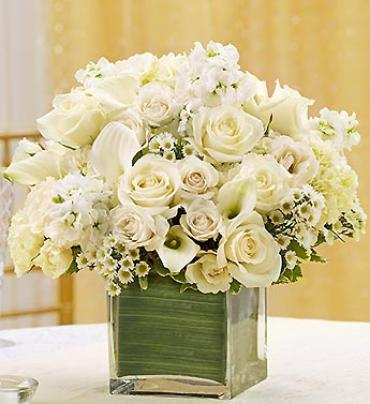 White roses and calla lilies arranged in a clear square vase